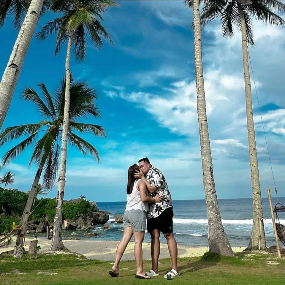 Earvin and Plexy kissing on the beach under palm trees